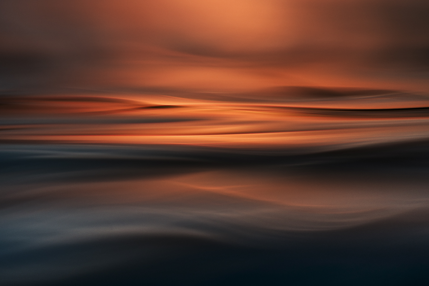 Abstract style ocean image at sunset, with warm orange and deep blue tones capturing silky water and glowing light.