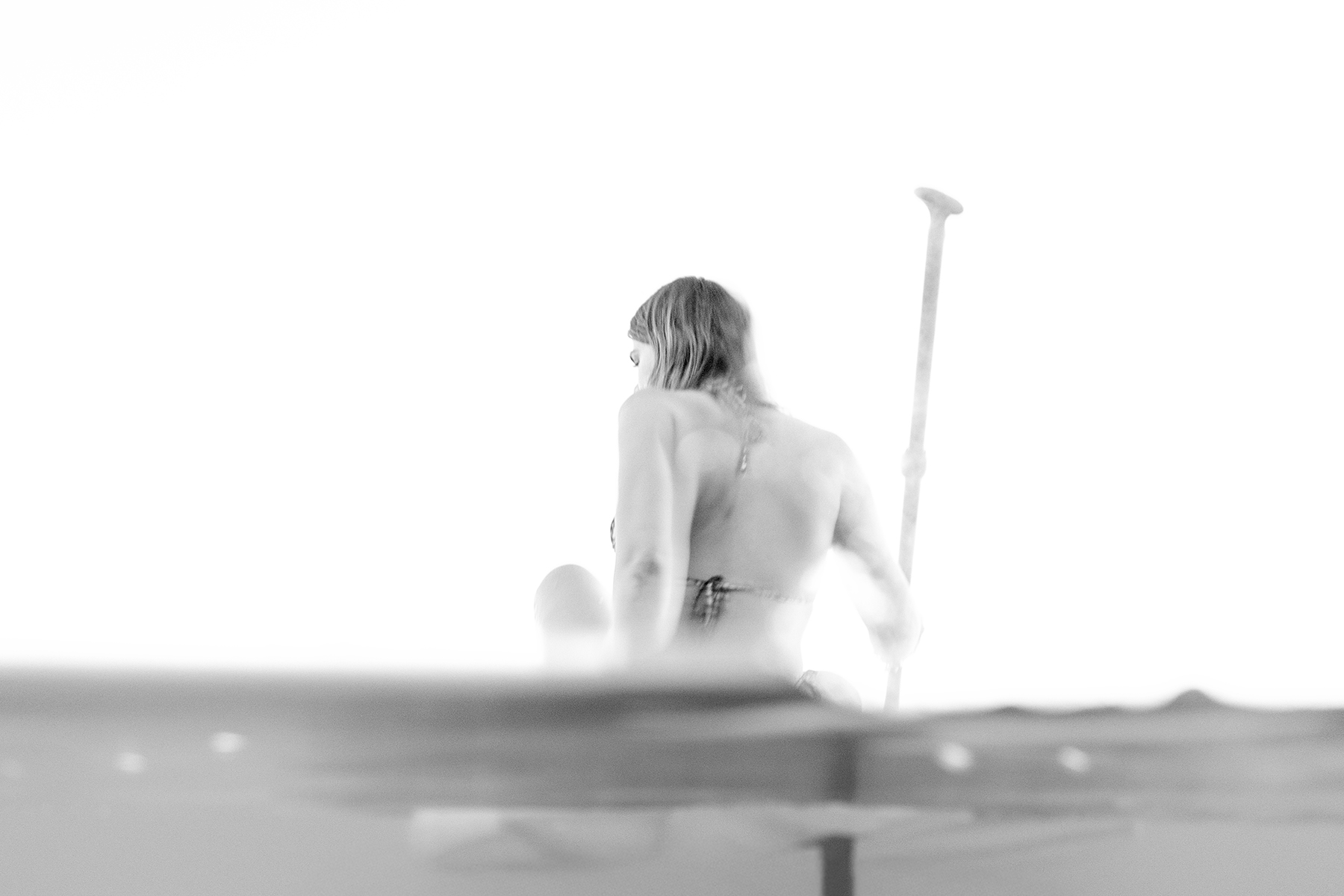 Black-and-white image of a person paddleboarding, viewed from behind the waterline.